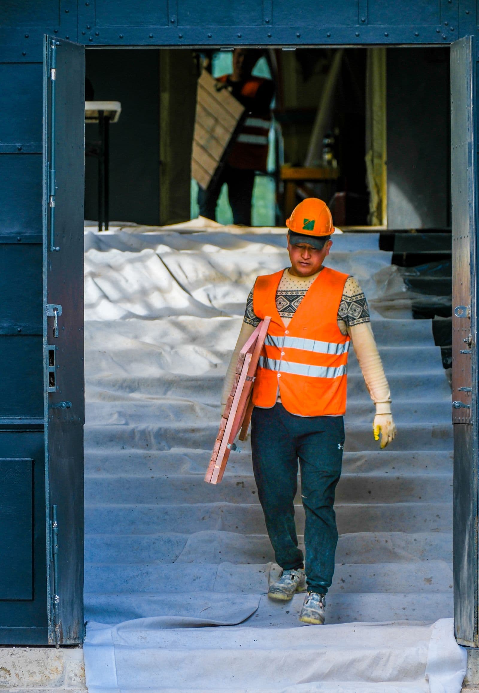 Worker in a safety vest carrying materials out of a building under renovation