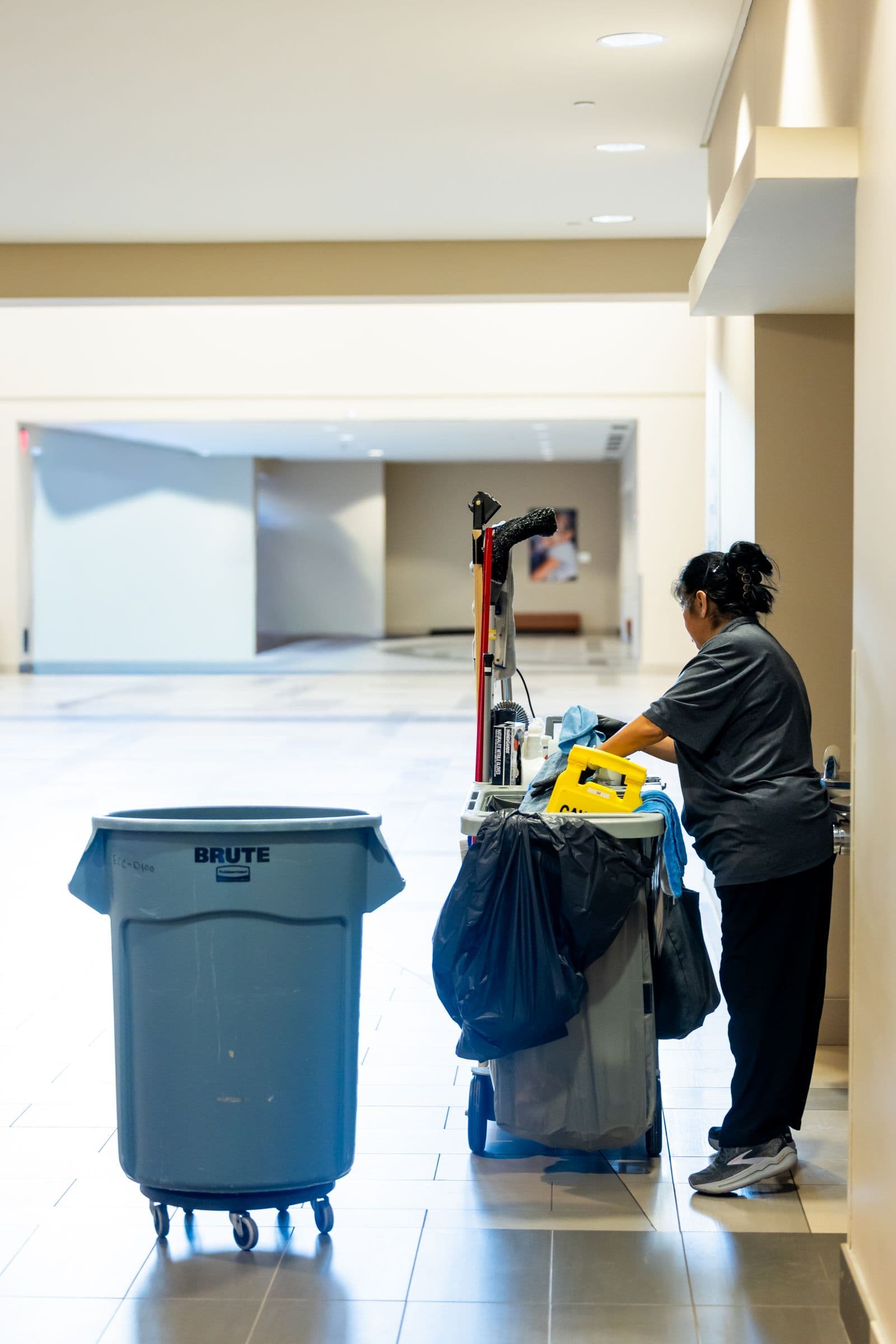 Janitorial worker pushing a cleaning cart through a commercial hallway